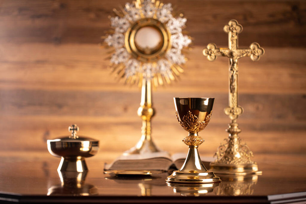 Catholic religion concept. Catholic symbols composition. The Cross, monstrance,  Holy Bible and golden chalice on brown background.  - Photo, Image