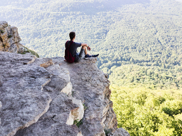Adam uçurumun kenarındaki bir kayanın üzerinde oturuyor. Yüksek kalite fotoğraf - Fotoğraf, Görsel