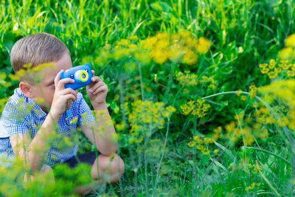 青いシャツにきれいな髪型のかわいい就学前の男の子は暑い夏の日に緑の植物の写真を撮ります。選択的フォーカス。肖像画 - 写真・画像