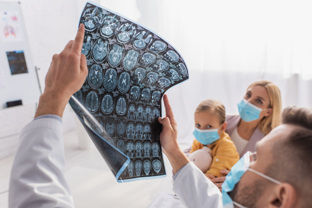 Blurred pediatrician holding mri scan near mother and kid in medical masks  - Foto, Imagem