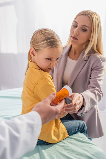 Blurred pediatrician holding jar with pills near mother and disgusted patient  - Zdjęcie, obraz