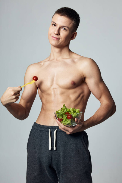 Şişirilmiş karın kasları olan atletik bir adam. Tabak çalışmasında sağlıklı salata. - Fotoğraf, Görsel