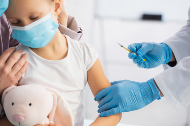 Pediatrician holding syringe near kid and parent in clinic  - Fotografie, Obrázek