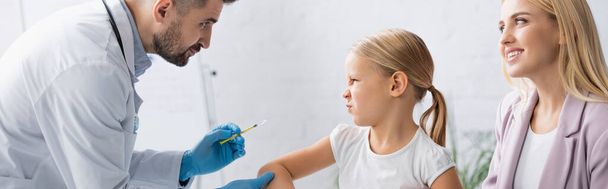 Doctor holding syringe near kid grimacing and smiling woman, banner  - Фото, изображение