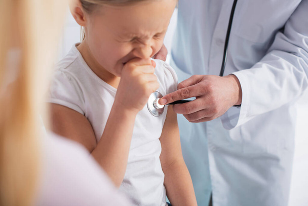 Pediatrician using stethoscope near diseased child in hospital  - Photo, Image