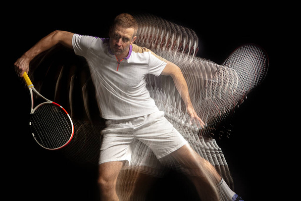 Power and speed. Young man, professional tennis player in motion and action isolated on dark background with stroboscope effect. - 写真・画像