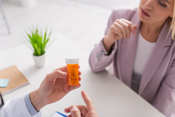 partial view of doctor pointing at container with pills near blurred woman - Foto, afbeelding