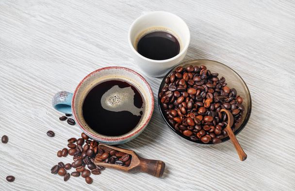 Köstlicher frischer Kaffee. Kaffeetassen und Kaffeebohnen auf hellem Holzhintergrund. - Foto, Bild