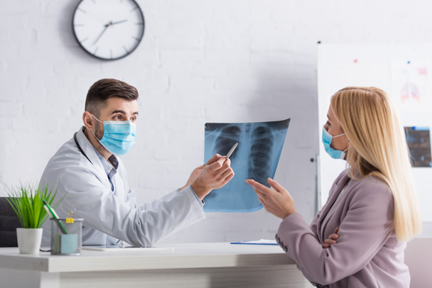 Arzt und Patient in medizinischen Masken zeigen während der Konsultation in der Klinik auf eine Fluorographie-Aufnahme - Foto, Bild