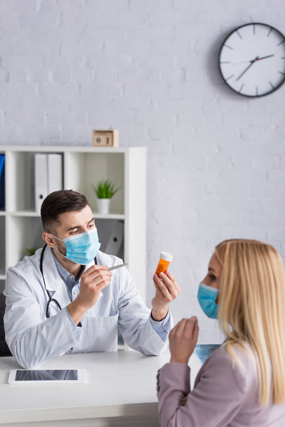 врач в медицинской маске указывает на таблетки возле блондинки - Фото, изображение