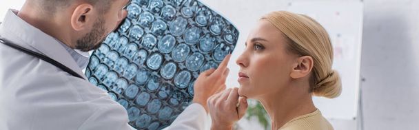 ανήσυχος γυναίκα κοιτάζοντας γιατρό κρατώντας τομογραφία εγκεφάλου, πανό - Φωτογραφία, εικόνα