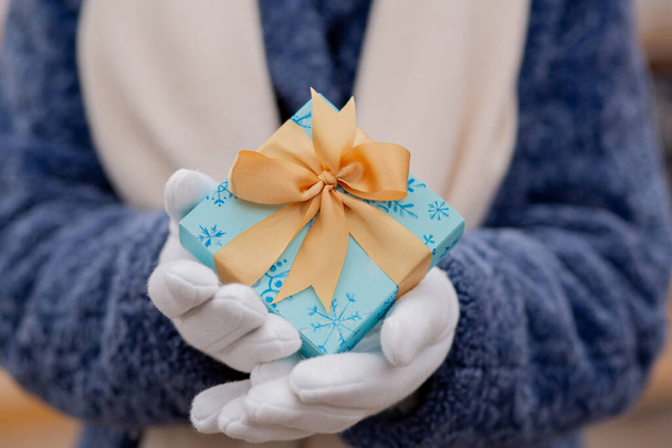 Woman dressed in a blue winter coat holding a small gift box with a silk ribbon at the street - Photo, Image