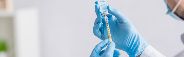 Teilaufnahme des Arztes in blauen Latexhandschuhen, die Spritze mit Coronavirus-Impfstoff füllen, Banner - Foto, Bild