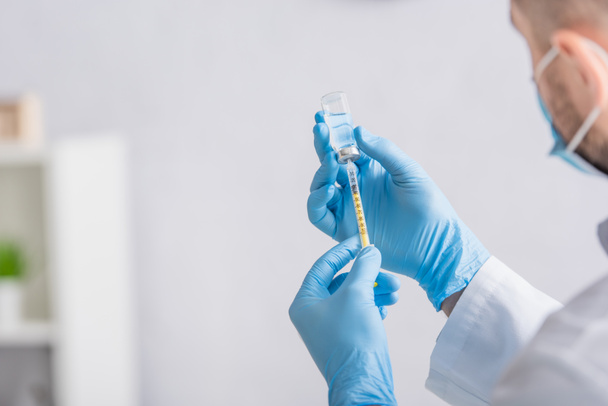 Ausgeschnittene Ansicht eines Arztes in Latexhandschuhen, der Spritze mit Impfstoff füllt - Foto, Bild