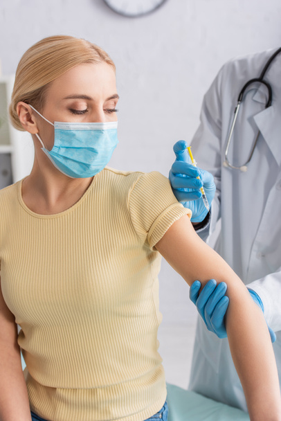врач в латексных перчатках вакцинирует женщину в медицинской маске в больнице - Фото, изображение
