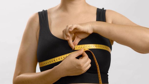 Mulher branca em sutiã esporte preto medindo seu peito com uma fita adesiva. Estúdio de alta qualidade foto no fundo branco. - Foto, Imagem