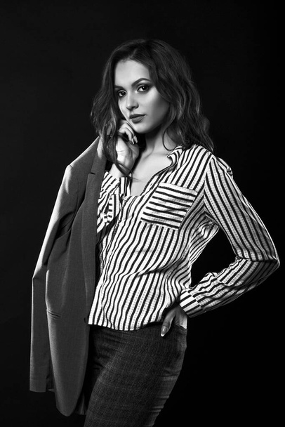 Πανέμορφη μελαχρινή γυναίκα φοράει πουκάμισο και αντρικό μπουφάν στο στούντιο με δραματικό φως. Ασπρόμαυρο πορτρέτο - Φωτογραφία, εικόνα