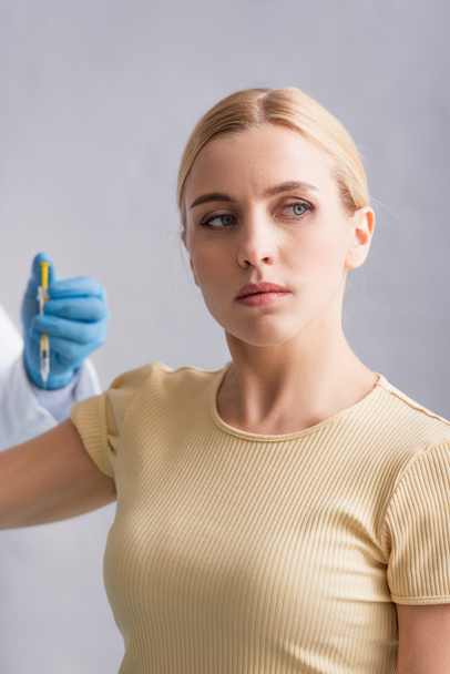 blondynka odwracając wzrok podczas wstrzykiwania szczepionki przez lekarza - Zdjęcie, obraz