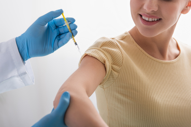 περικοπή άποψη του γιατρού σε γάντια λατέξ δίνοντας ένεση του εμβολίου σε χαμογελαστή γυναίκα - Φωτογραφία, εικόνα