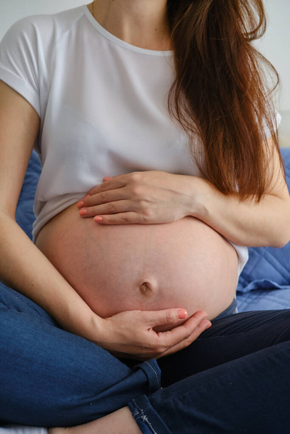 Close up shot of young pregnant woman stands by the window and hugs her belly with her hands Vewrsion 3 - Foto, afbeelding
