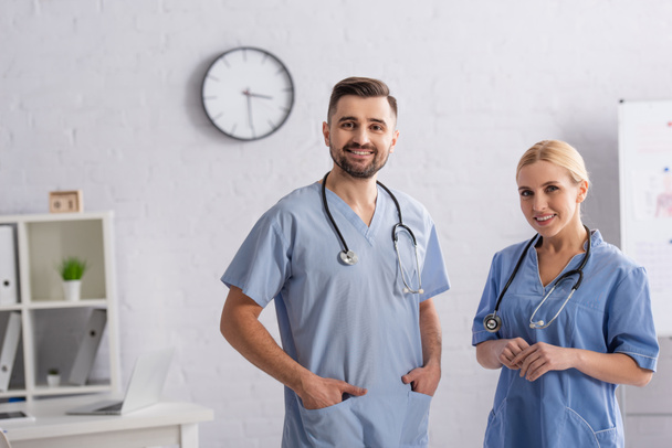 Arzt steht mit Händen in Uniformtaschen neben lächelndem Kollegen - Foto, Bild