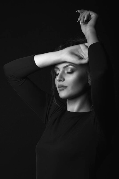 Dramatický portrét unavené mladé ženy nosí černé šaty pózující v tmavé místnosti. Černobílý portrét - Fotografie, Obrázek