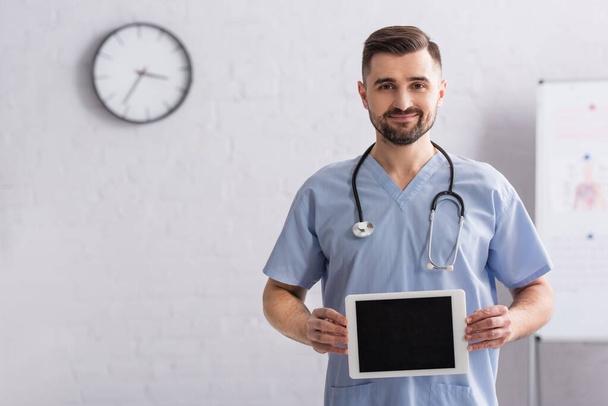 pleased doctor in blue uniform holding digital tablet with blank screen - Zdjęcie, obraz