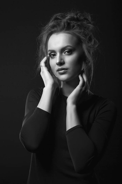 Dramatic portrait of a glamorous young woman wears black dress posing in a dark room. Black and white portrait - Фото, зображення