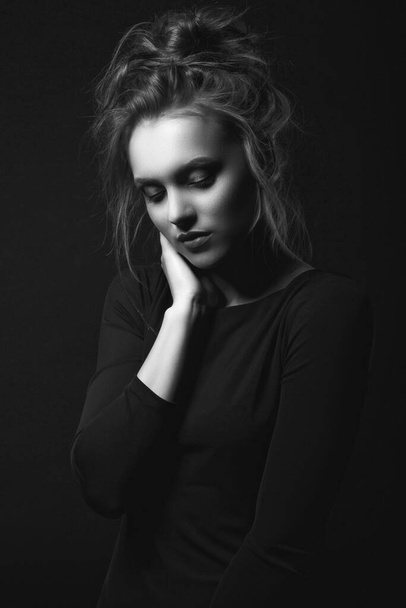 Dramatic portrait of a sad beautiful woman wears black dress posing in a dark room. Black and white portrait - Photo, image