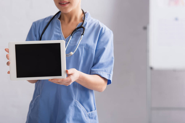 vista recortada del médico en azul uniforme celebración tableta digital con pantalla en blanco - Foto, imagen
