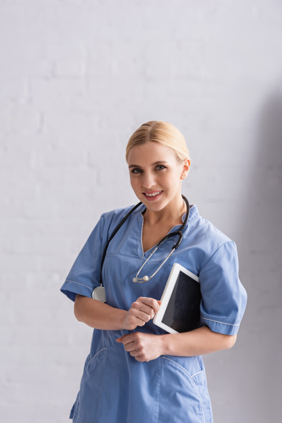 pretty doctor in blue uniform smiling at camera while holding digital tablet - Photo, Image