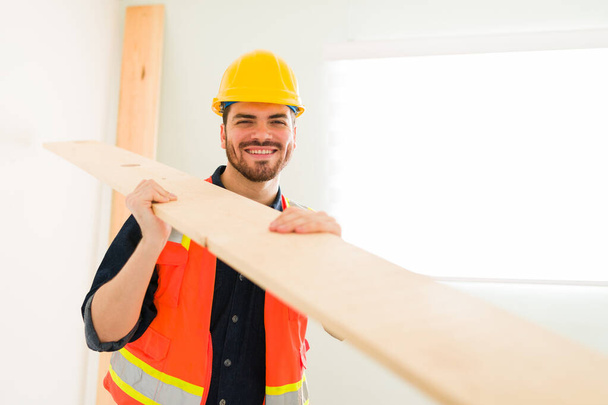 Buona giornata di lavoro. Ritratto di un attraente appaltatore sorridente mentre tiene in mano una barra di legno per costruire una nuova casa - Foto, immagini
