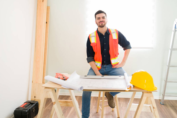 Περήφανος εργολήπτης που απολαμβάνει μια μέρα στη δουλειά και ελέγχει τα σχέδια κατά τη διάρκεια της κατασκευής ενός νέου σπιτιού  - Φωτογραφία, εικόνα