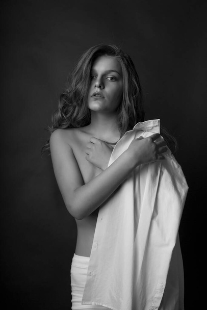 Seductive blond model wears white men's shirt and posing with naked shoulders at studio. Monochrome shot - Foto, immagini