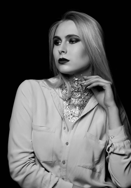 Luxurious blond model posing at studio with bright makeup and foil on her neck. Monochrome shot - Foto, afbeelding