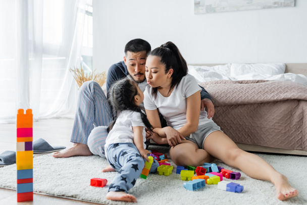asian parents pouting lips near toddler daughter and building blocks  - Zdjęcie, obraz