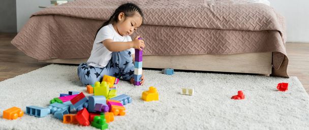 asian toddler girl playing building blocks on carpet in bedroom, banner - 写真・画像