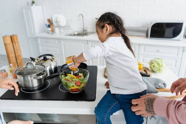 asian kid seasoning salad near parents in kitchen  - Foto, immagini