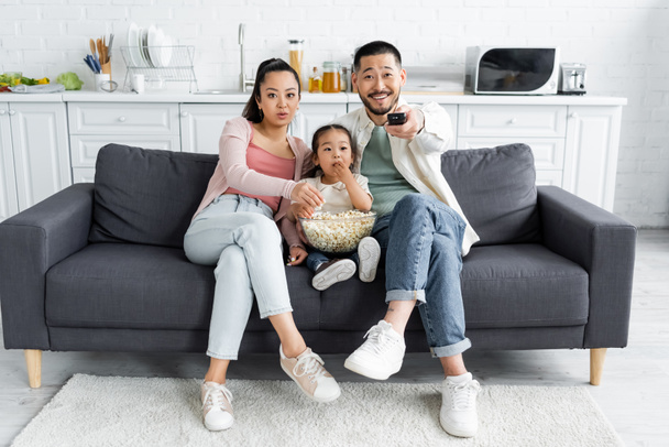 Азиатская семья смотрит телевизор и ест попкорн в гостиной - Фото, изображение