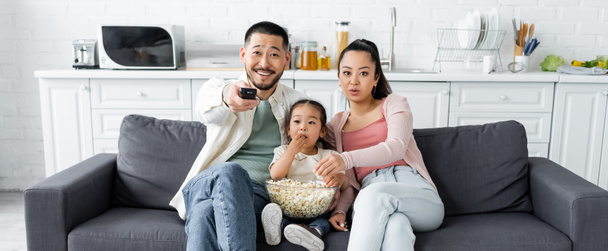asian family watching tv and eating popcorn in living room, banner - Foto, Bild