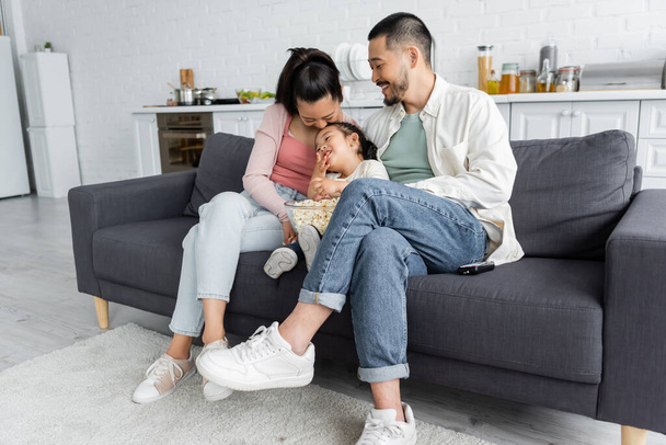 happy asian family watching movie near popcorn in living room - Foto, afbeelding