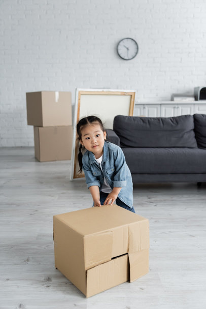 aziatische peuter meisje duwen kartonnen doos in nieuw huis - Foto, afbeelding