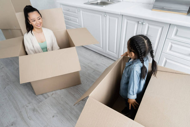 cheerful asian mother looking at toddler daughter in carton box - Photo, image