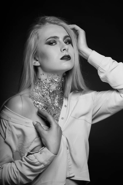 Черно-белая фотосессия красоты: стройная модель позирует в студии с ярким макияжем и фольгой на шее - Фото, изображение