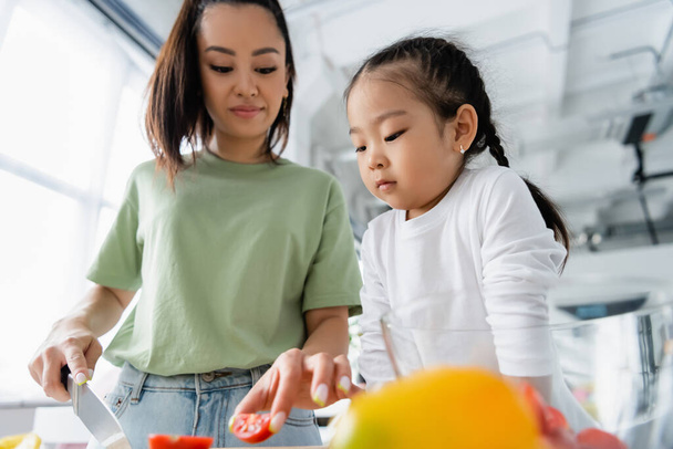 happy asian mother holding knife while preparing salad near daughter  - Foto, Bild
