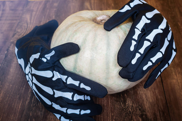 Decorazione di Halloween su uno sfondo di legno. I guanti di scheletro tengono una zucca - Foto, immagini