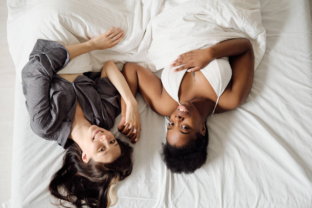 複数人種のレズビアンカップルが毛布の下に横たわって - 写真・画像