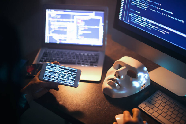 Hacker avec téléphone portable en utilisant des ordinateurs dans la chambre noire - Photo, image
