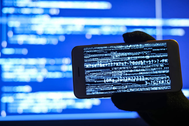 Hacker mit Handy nahe Bildschirm des Computers - Foto, Bild