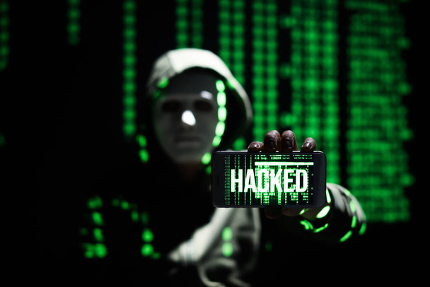 Хакер держит мобильный телефон со словом Взломанный на экране на темном фоне - Фото, изображение